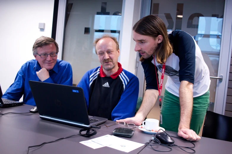 two men and a woman are looking at a laptop