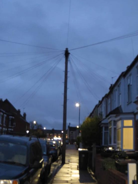 a street in an older city at dusk with many cars parked along the road