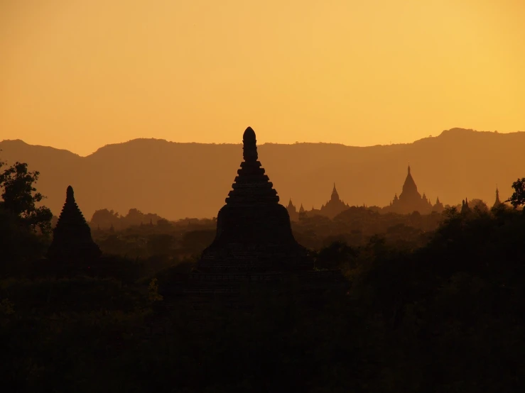 a sunset view of a buddhist temple with a mountain range in the background