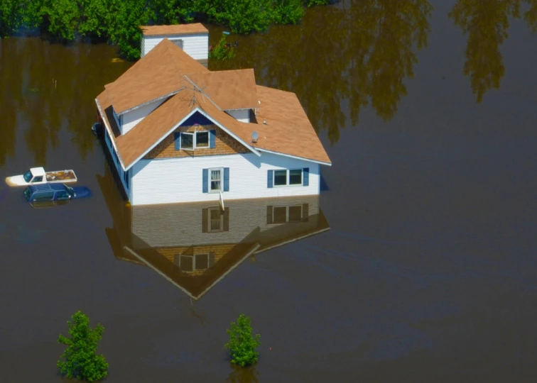 a house sits on a flooded bank and is surrounded by flood water