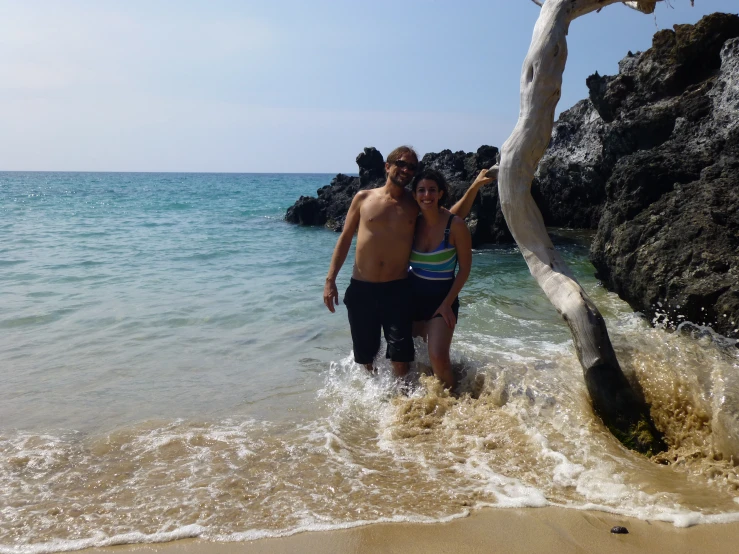 a man and a woman pose at the edge of the water near an old tree