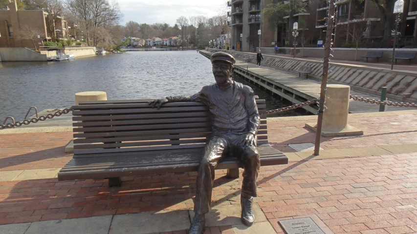 a statue sitting on a wooden bench overlooking the water