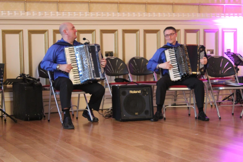 two men sitting down while holding an instrument