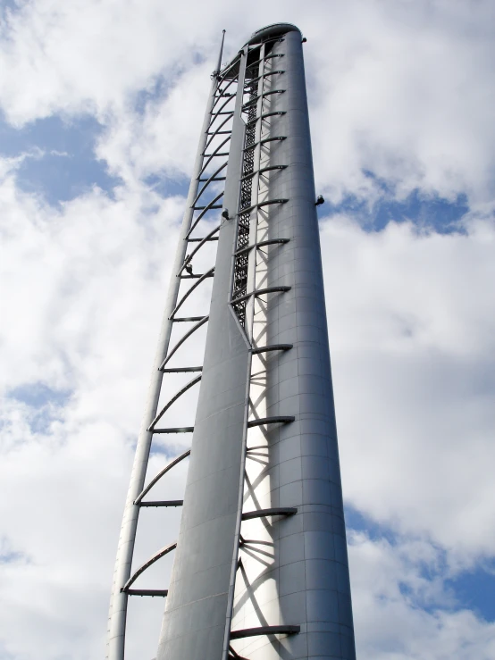 a tall tower with metal pipes is standing in front of a cloudy blue sky