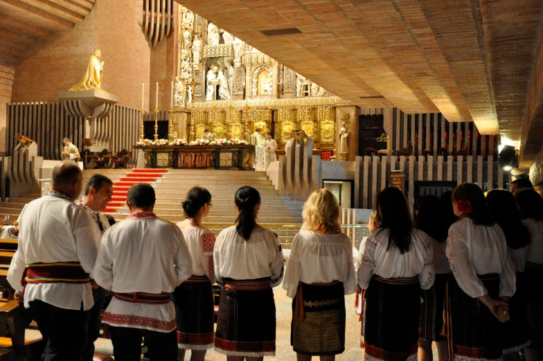 people wearing traditional clothes look at a priest from the back