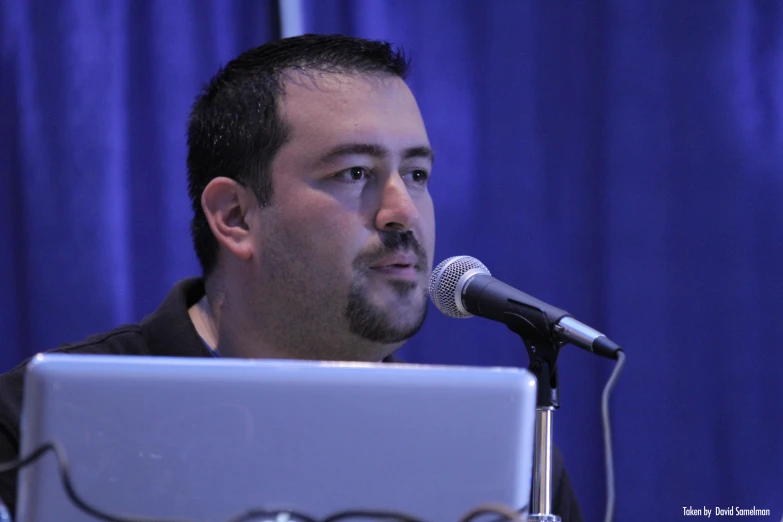 a man with black hair and beard speaking into a microphone