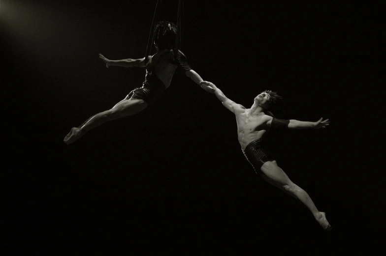 an acrobatic man and woman in black performing a stunt on a dark surface