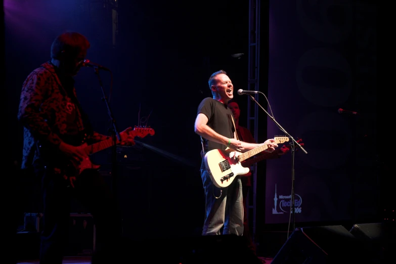 a man on stage sings into a microphone and guitar