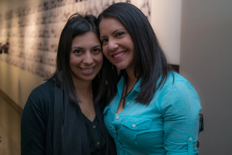 two women smile for the camera in front of a wall of words