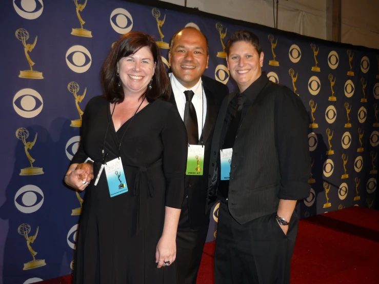 three people on a red carpet and one is wearing a black suit