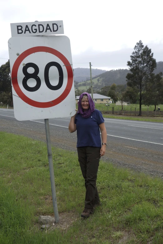 a woman poses next to a speed limit sign