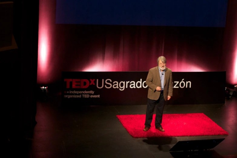 an older man standing on a stage with the ted usbaraad sign in the background