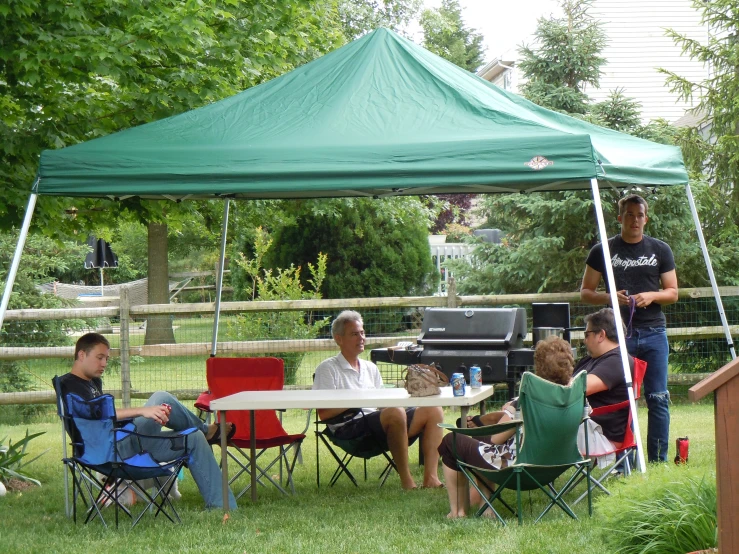 people sitting at tables under a green tent while a man speaks on a phone