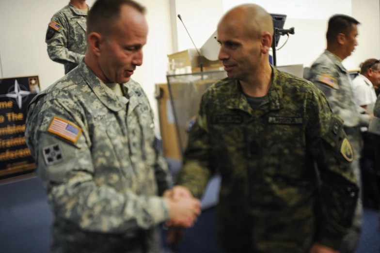 two soldiers shaking hands in a room with other people