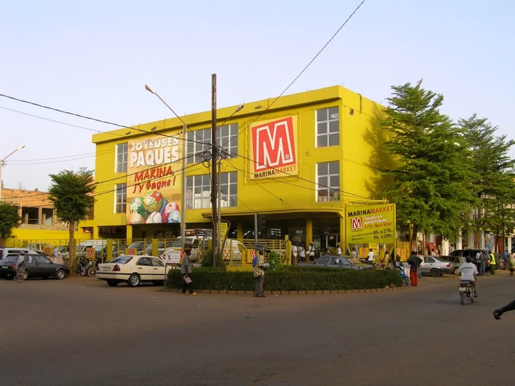 people walk around a street corner with a car in front of a yellow building