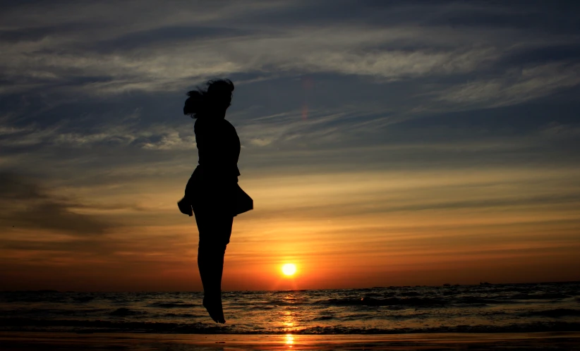 a girl is jumping at sunset on the beach