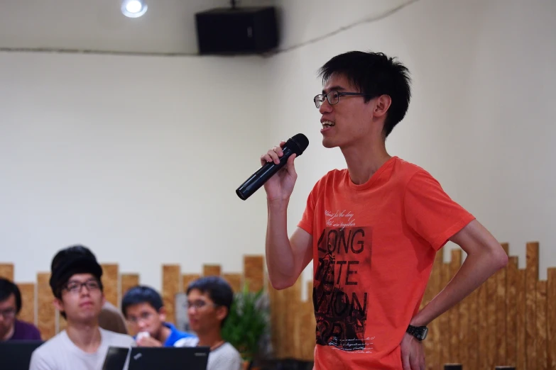 an asian man wearing a red shirt holds a microphone