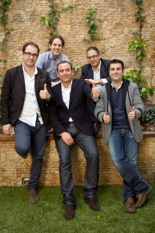 four young men pose together in front of a brick wall