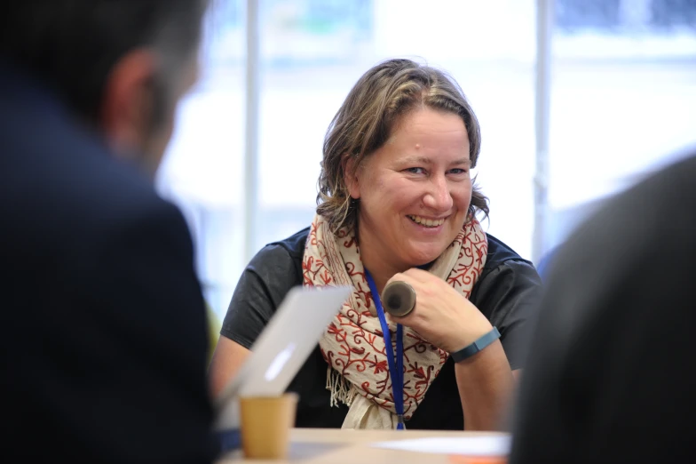 a woman sits talking into a microphone while a man listens