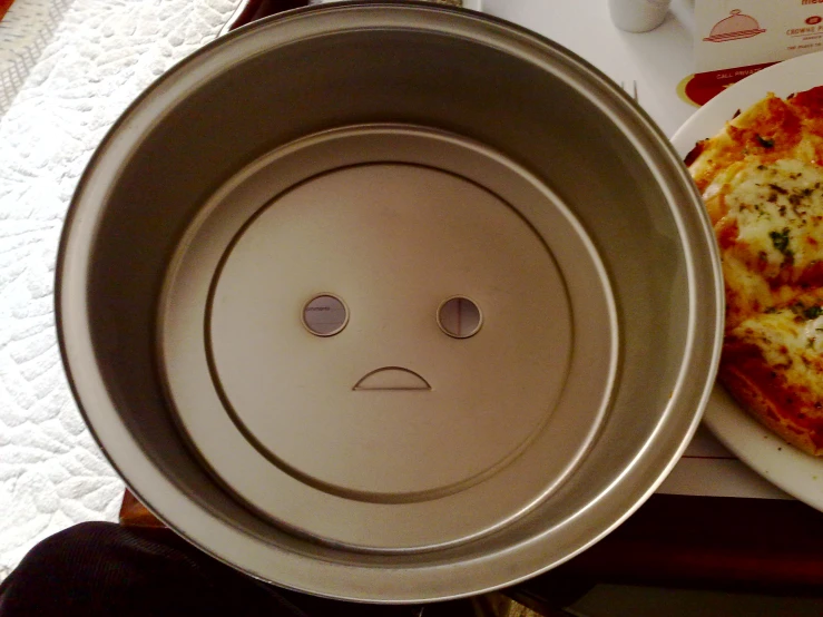 a pizza pan with a sad face on it next to two plates of pizza