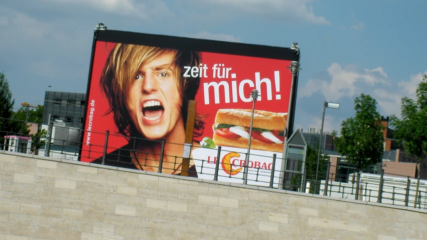 a billboard featuring the face of a young man with mouth open, a large sandwich in front of him