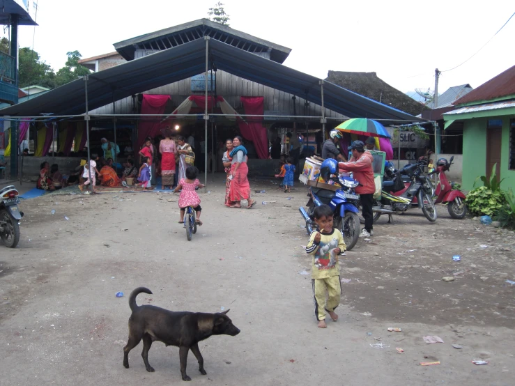 there are people in front of a large building with a small black dog walking near a black and white dog