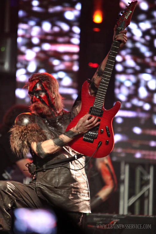 a man with black makeup and a red guitar on stage