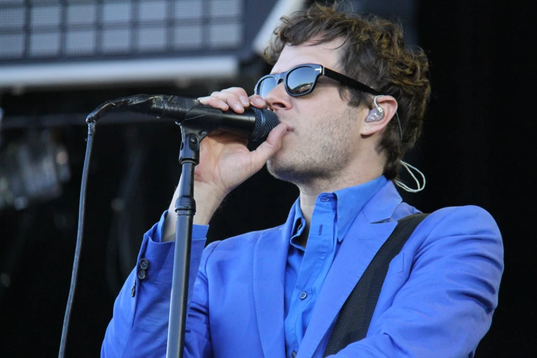 man in sunglasses and a blue shirt singing into a microphone