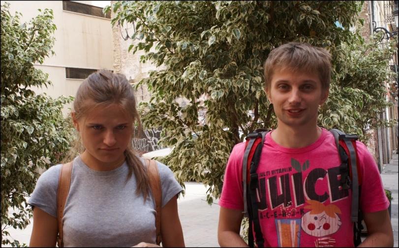 two people on the sidewalk in front of a tree