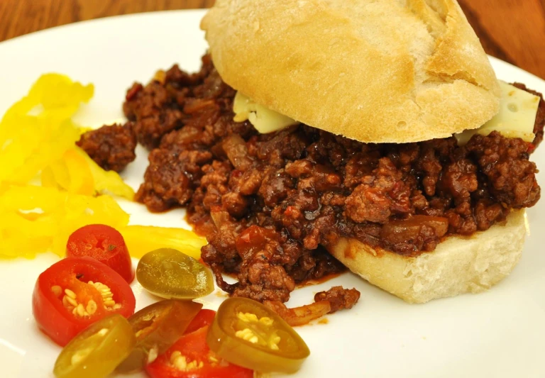 a sloppy joe sandwich is served with a side of pickles and tomato slices