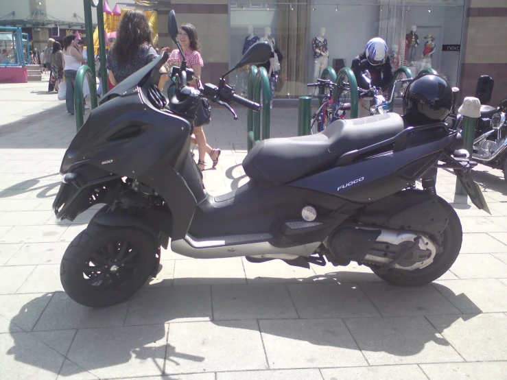 people walk and talk by several parked motor bikes