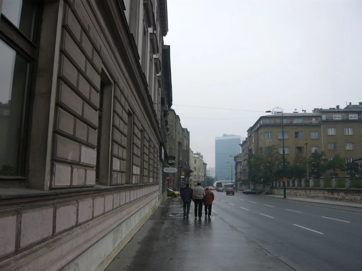 some people are walking down the sidewalk in the rain