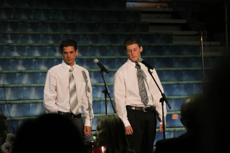 two men wearing white shirts and tie standing next to microphones