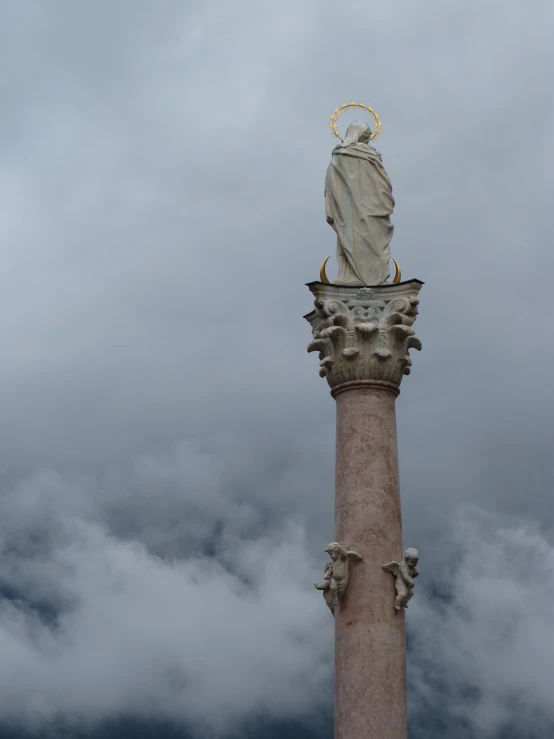 a statue sitting on top of a pink pillar surrounded by clouds