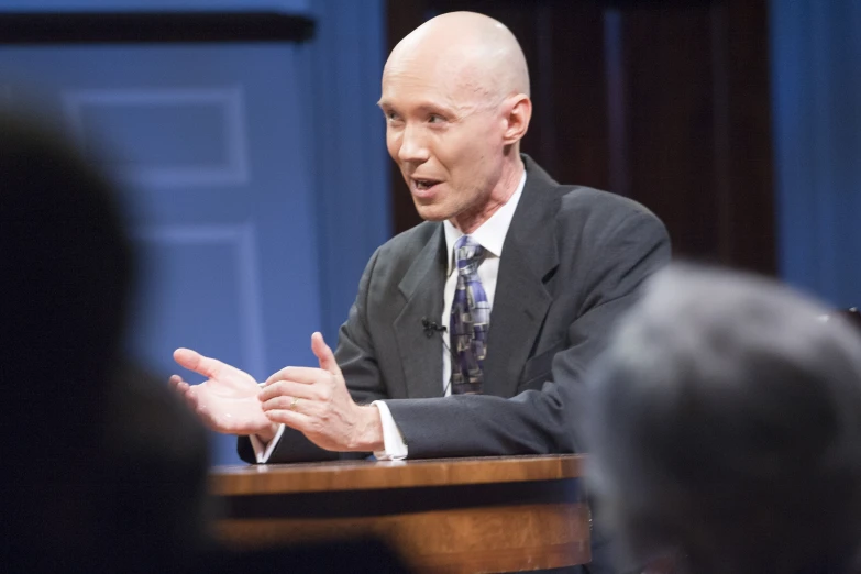 a man with a bald head speaking at a conference