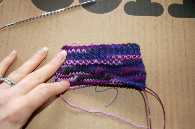 woman's hands sewing a colorful piece of material on a cardboard box