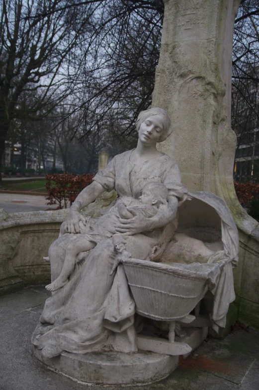 a statue of a woman holding a child in a basin next to a tree