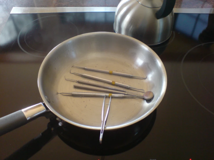 a pan sitting on a stove with four small tools sticking out of it
