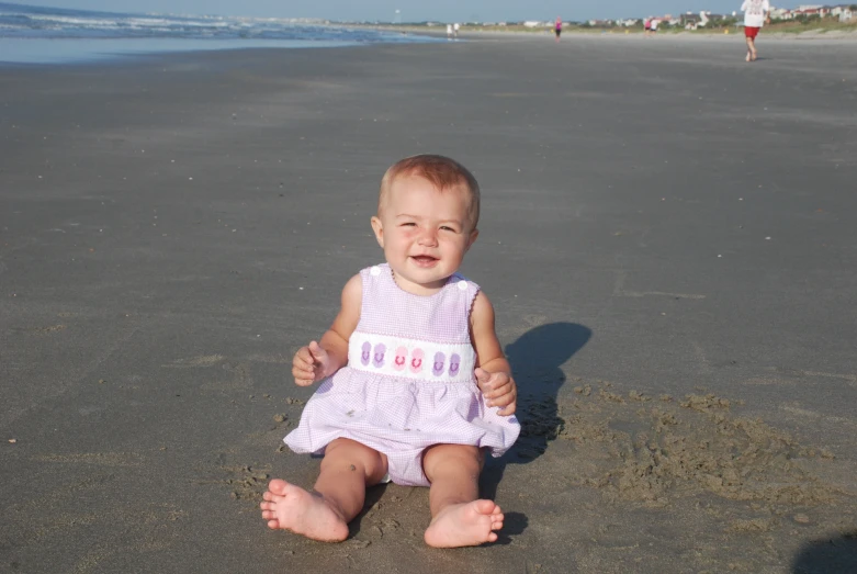 a baby girl sitting on the beach in front of a beach house