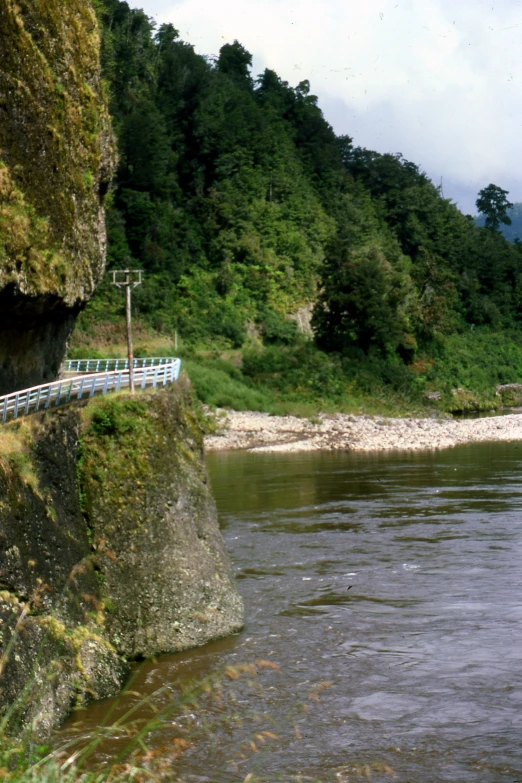 a narrow bridge crossing the water next to a mountain