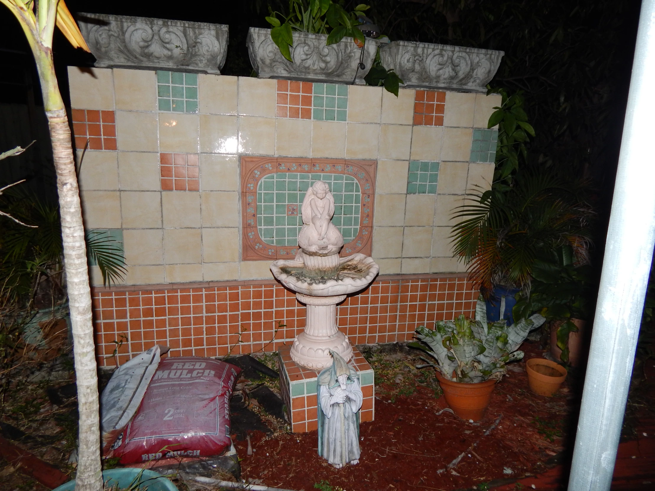 small fountain and plant in front of the orange tiled wall