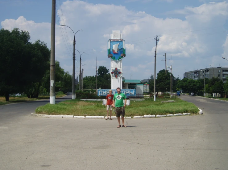 two people in green shirts stand in front of a tall tower with a clock on it