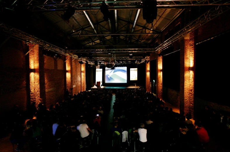 a dark room filled with people watching a large screen