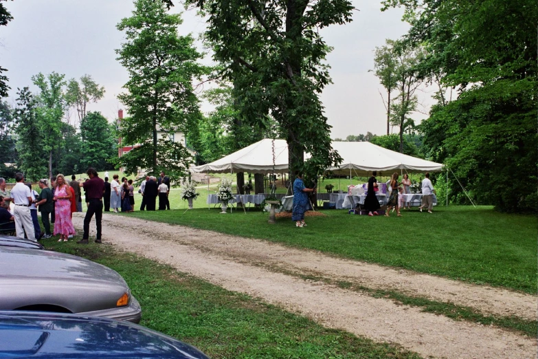 a group of people standing on a dirt road near tents and picnic tables