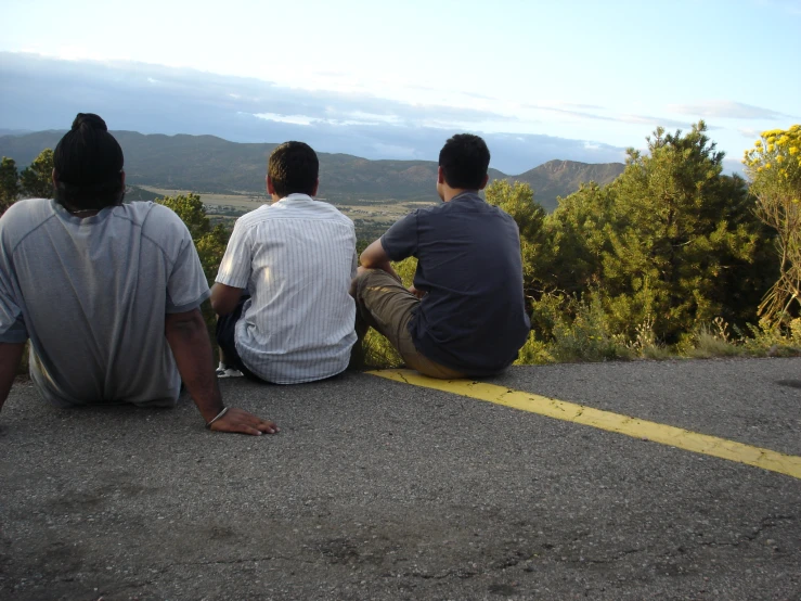 a group of three men sitting next to each other on the side of a road