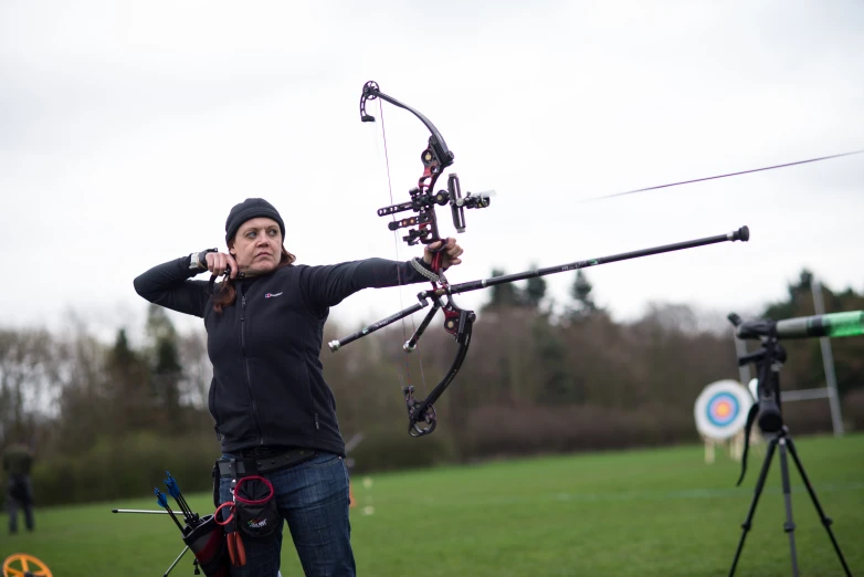 woman aiming at target with an arrow and bow in a field