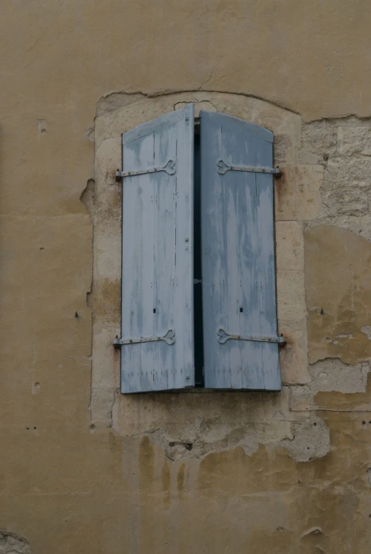 a brown stone wall with two blue wooden shutters on each side and one blue shutter