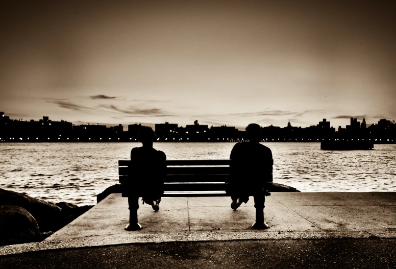 a couple sitting on a park bench next to a body of water