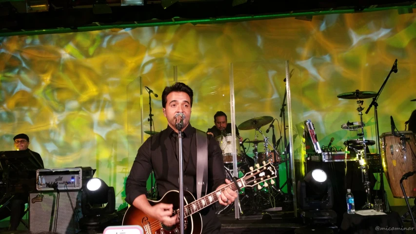 a man standing on top of a stage holding an acoustic guitar