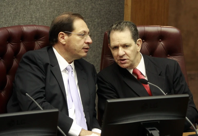 two men sit in a chair, facing one another, with their eyes open